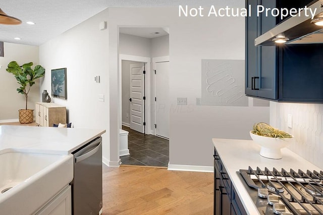 kitchen with a textured ceiling, light countertops, appliances with stainless steel finishes, under cabinet range hood, and light wood-type flooring