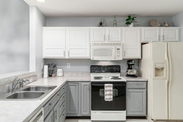 kitchen with a sink, light countertops, white appliances, and gray cabinets