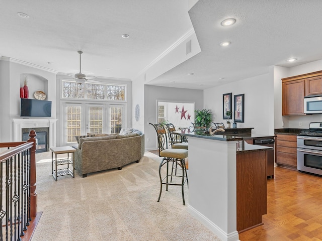 kitchen featuring a kitchen bar, ornamental molding, dark countertops, open floor plan, and appliances with stainless steel finishes