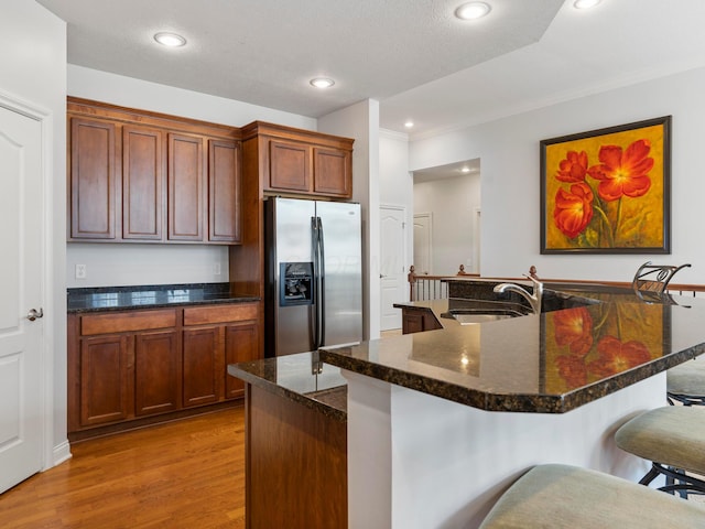 kitchen featuring light wood finished floors, a breakfast bar, recessed lighting, a sink, and stainless steel refrigerator with ice dispenser