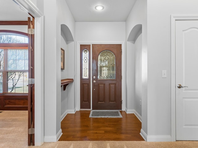 foyer with baseboards, arched walkways, and wood finished floors