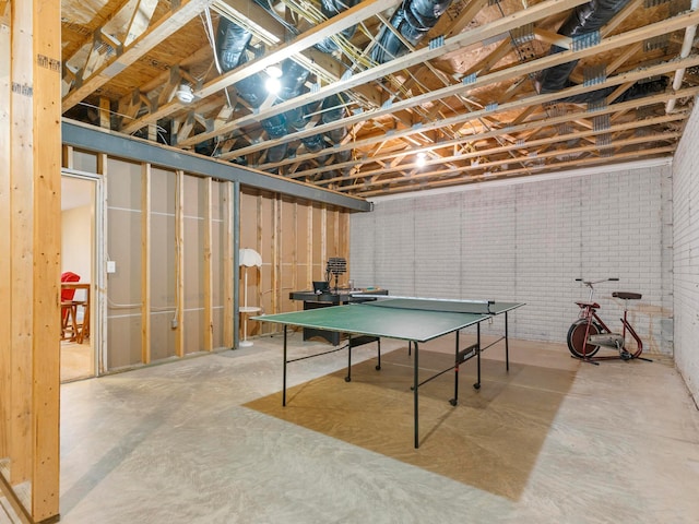 recreation room featuring brick wall and concrete flooring