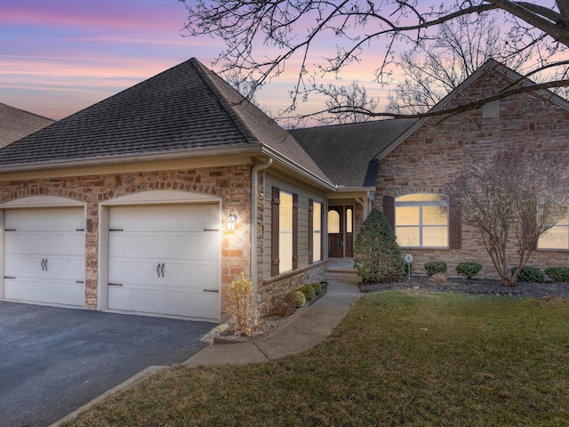 property exterior at dusk featuring a lawn, aphalt driveway, stone siding, a shingled roof, and a garage