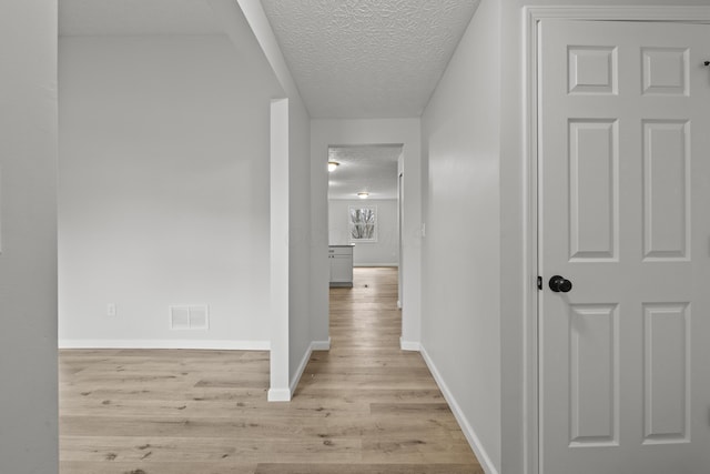 hallway with visible vents, light wood-style flooring, a textured ceiling, and baseboards