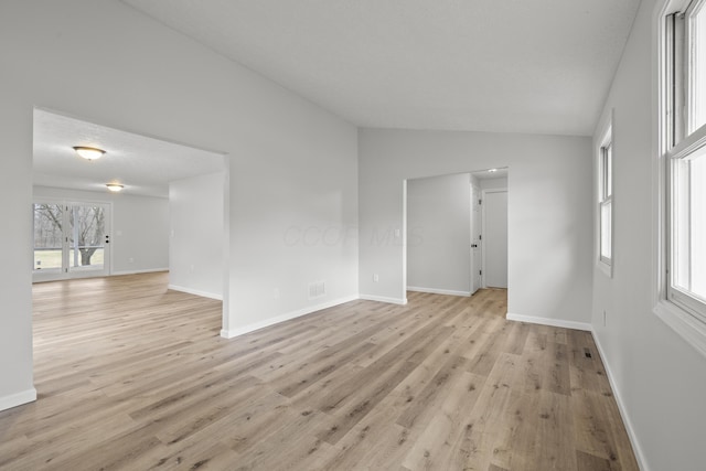 spare room with light wood-type flooring, baseboards, visible vents, and vaulted ceiling