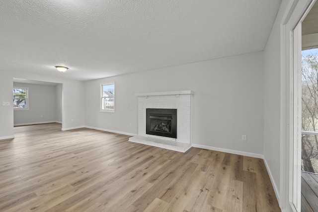 unfurnished living room featuring a brick fireplace, plenty of natural light, light wood-style flooring, and a textured ceiling