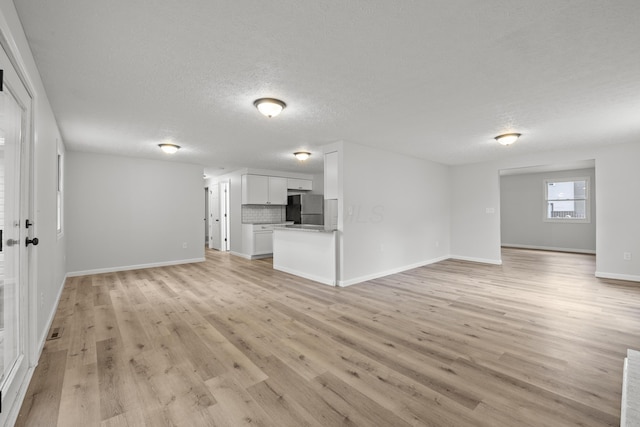 unfurnished living room featuring a textured ceiling, baseboards, and light wood-style floors