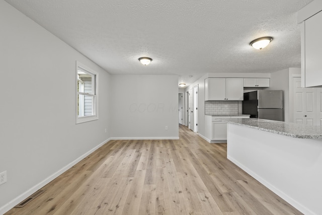 unfurnished living room featuring light wood finished floors, visible vents, a textured ceiling, and baseboards