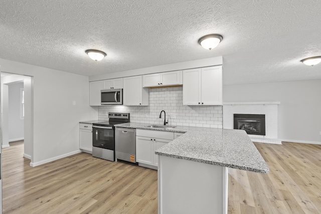 kitchen with tasteful backsplash, light wood-style flooring, a peninsula, stainless steel appliances, and a sink