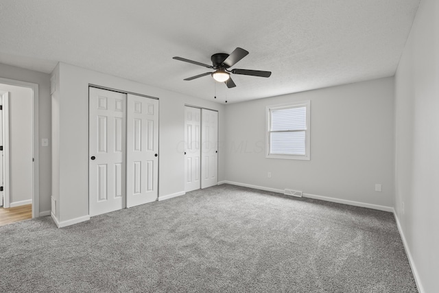 unfurnished bedroom featuring baseboards, multiple closets, a textured ceiling, and carpet flooring