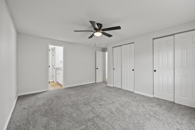 unfurnished bedroom featuring carpet flooring, baseboards, two closets, and a textured ceiling