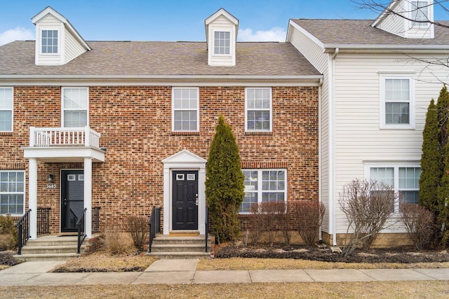 townhome / multi-family property with roof with shingles and brick siding