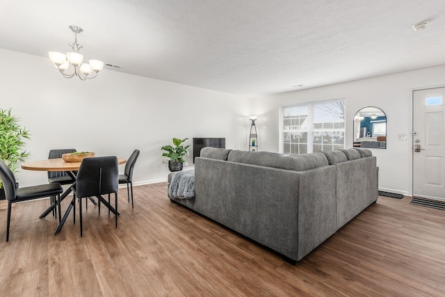 living area with baseboards, visible vents, a chandelier, and wood finished floors