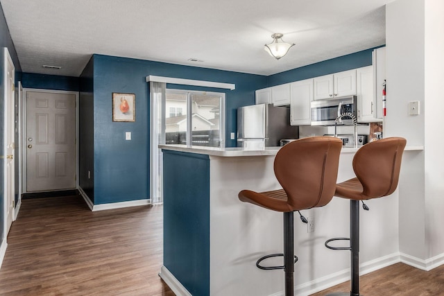 kitchen featuring a breakfast bar, wood finished floors, white cabinetry, light countertops, and appliances with stainless steel finishes