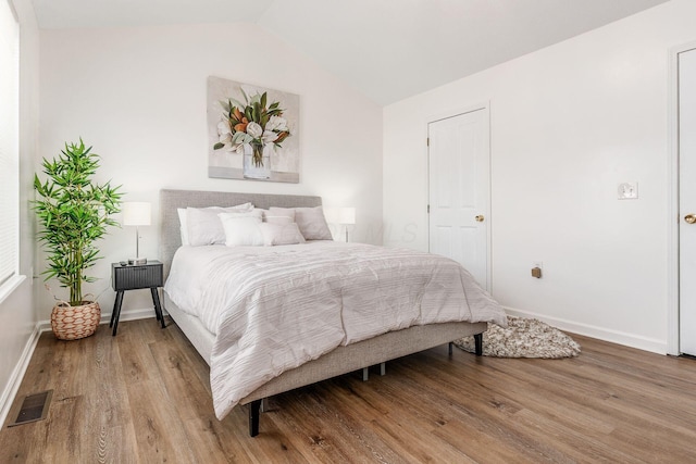 bedroom featuring lofted ceiling, baseboards, visible vents, and wood finished floors