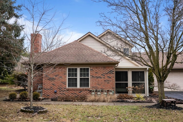 view of side of property featuring brick siding, a shingled roof, a sunroom, driveway, and a chimney