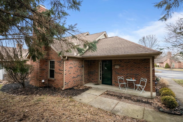 view of front of home with a patio area, brick siding, and roof with shingles