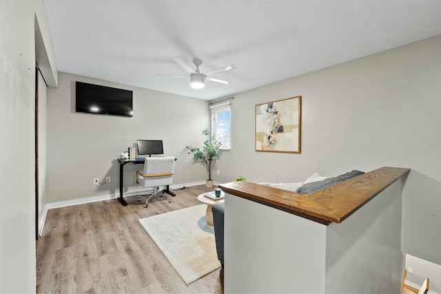 office space with a ceiling fan, light wood-type flooring, a textured ceiling, and baseboards