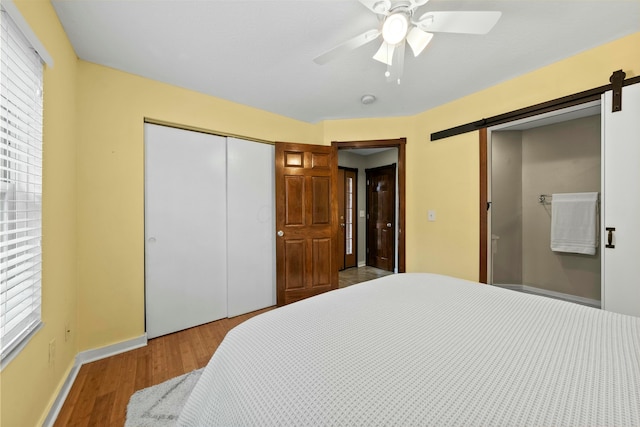 bedroom featuring a barn door, baseboards, a ceiling fan, wood finished floors, and a closet