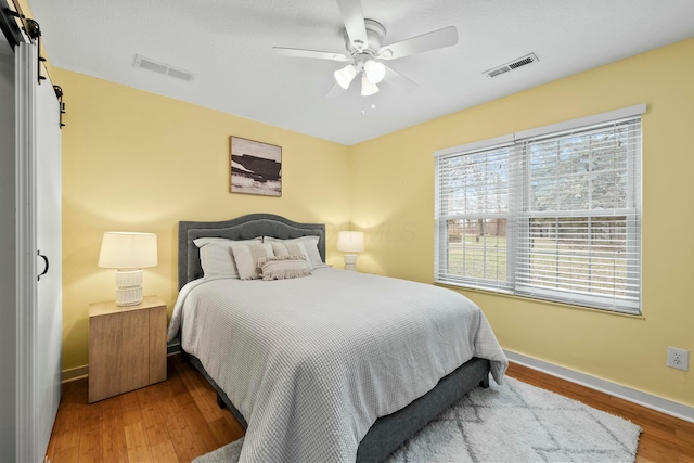 bedroom featuring a barn door, visible vents, baseboards, and wood finished floors