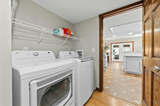 clothes washing area with laundry area, french doors, washing machine and dryer, and light wood-style floors