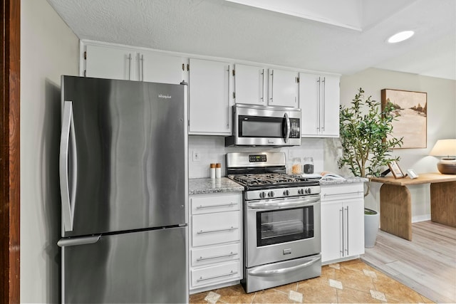 kitchen with appliances with stainless steel finishes, white cabinetry, a textured ceiling, and light stone countertops