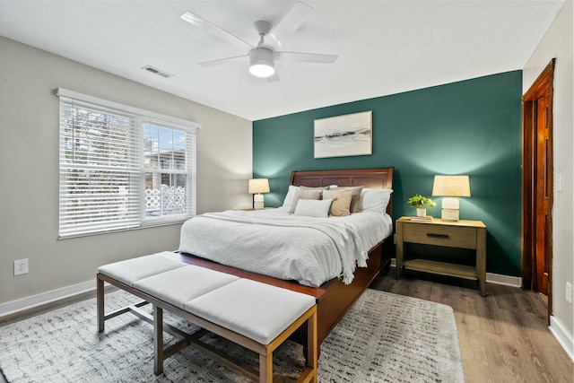 bedroom featuring ceiling fan, wood finished floors, visible vents, and baseboards