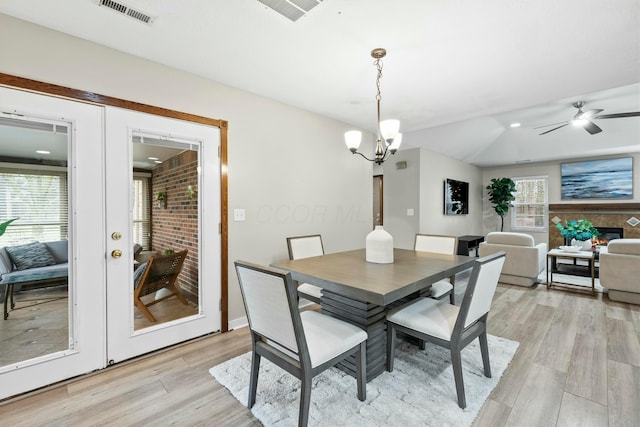 dining area featuring light wood-style flooring, ceiling fan with notable chandelier, visible vents, french doors, and a glass covered fireplace