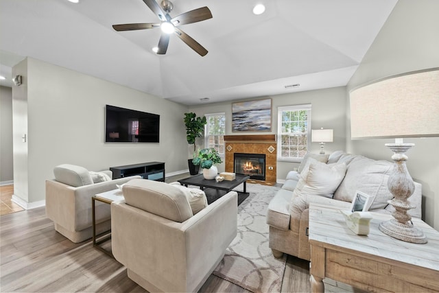 living room with vaulted ceiling, a tile fireplace, light wood-style flooring, and baseboards