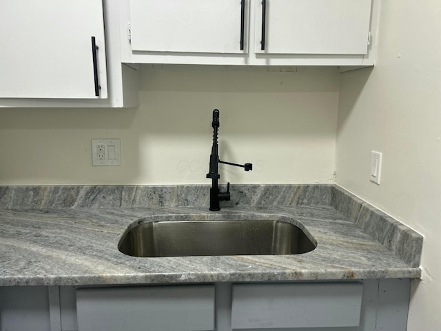 kitchen with a sink, light stone countertops, and white cabinets