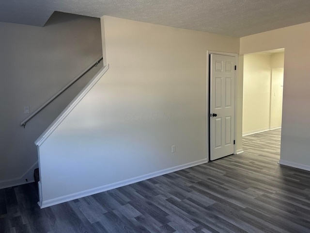 unfurnished room with baseboards, dark wood finished floors, and a textured ceiling