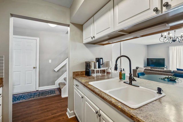 kitchen featuring dark wood-type flooring, white cabinetry, a sink, and baseboards