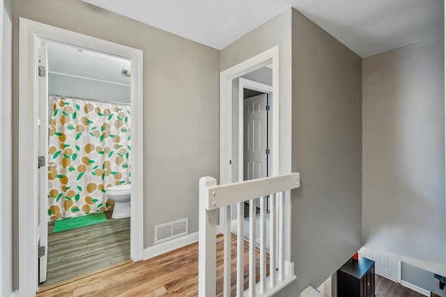 hall with baseboards, visible vents, wood finished floors, and an upstairs landing