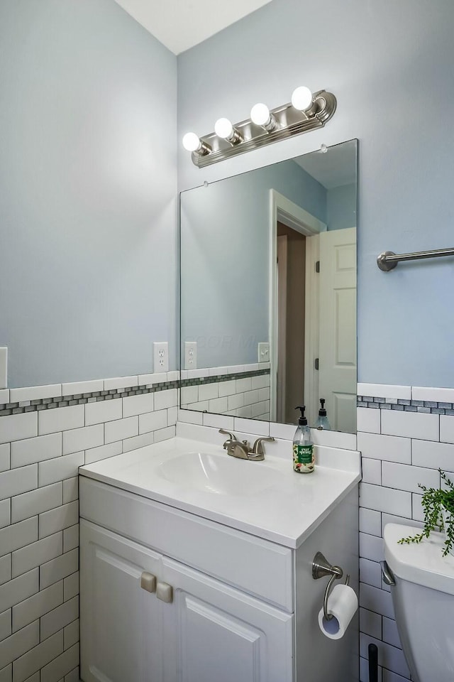 bathroom with toilet, vanity, tile walls, and wainscoting