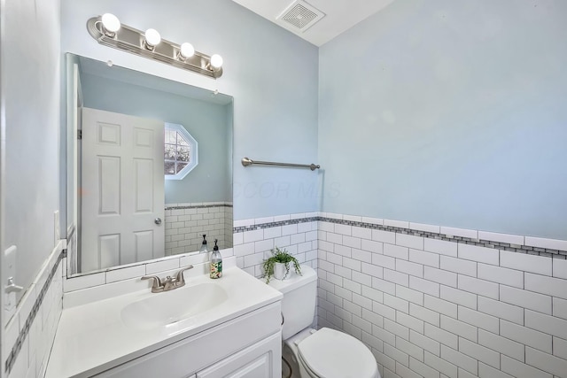 half bathroom featuring visible vents, wainscoting, toilet, vanity, and tile walls