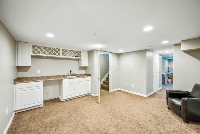 kitchen with light carpet, a sink, white cabinetry, and baseboards