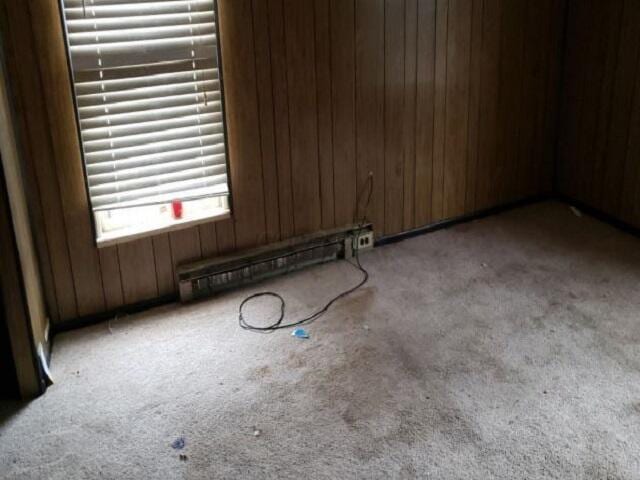 empty room with a baseboard radiator, carpet flooring, and wooden walls