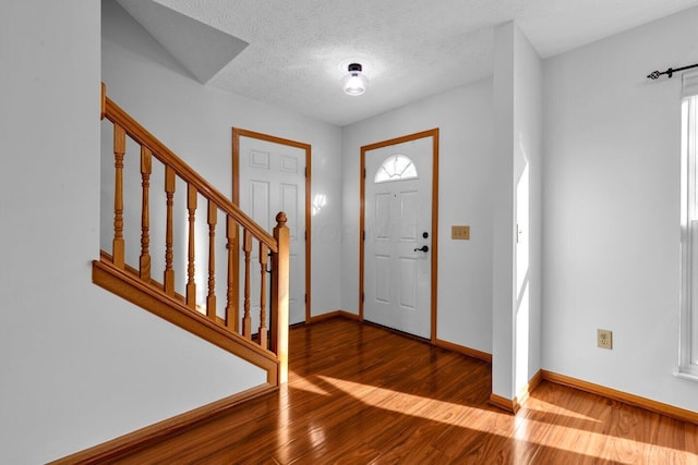 entryway with a textured ceiling, stairs, baseboards, and wood finished floors