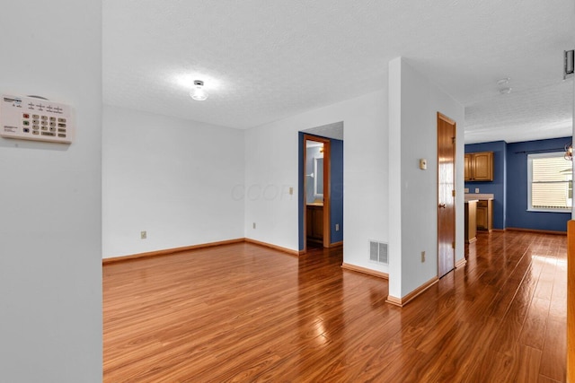 unfurnished room with a textured ceiling, wood finished floors, visible vents, and baseboards