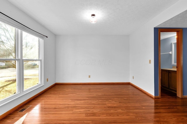 empty room featuring a wealth of natural light, baseboards, visible vents, and wood finished floors