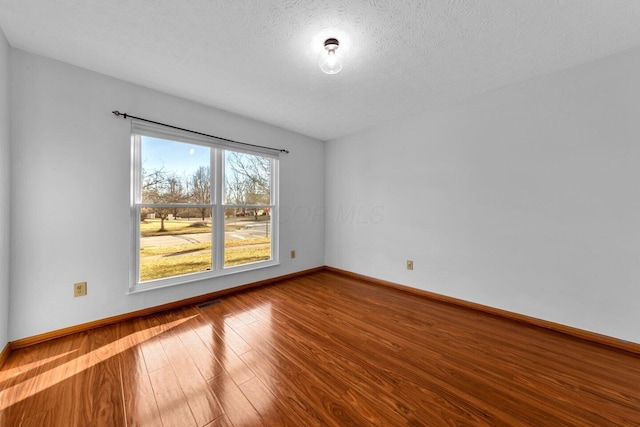 spare room featuring a textured ceiling, baseboards, and wood finished floors