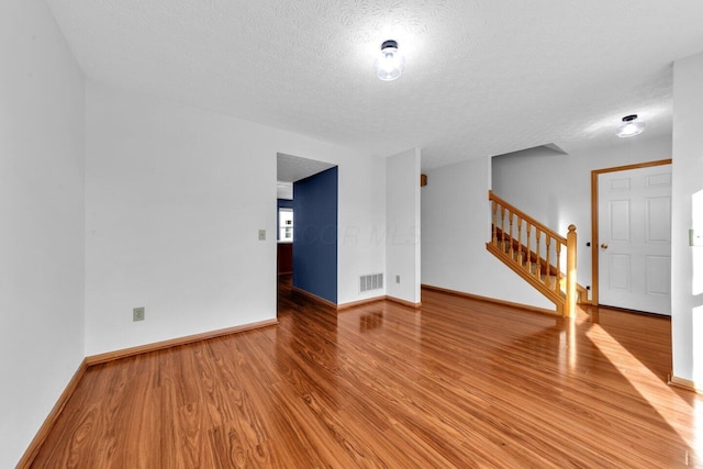 unfurnished living room with baseboards, visible vents, stairway, wood finished floors, and a textured ceiling