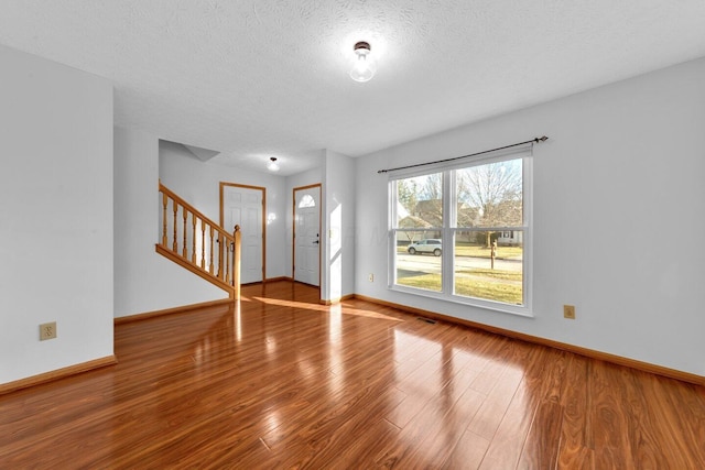 foyer with stairs, a textured ceiling, baseboards, and wood finished floors