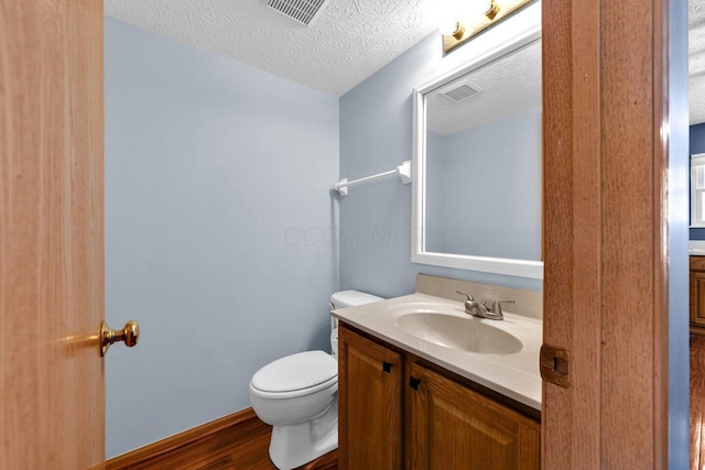 bathroom with visible vents, vanity, toilet, and a textured ceiling