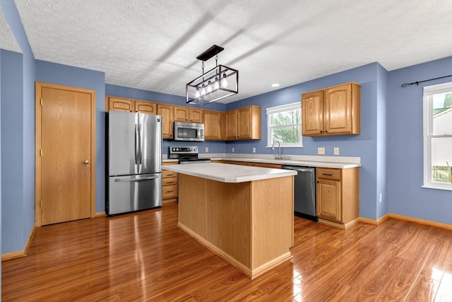 kitchen with stainless steel appliances, light countertops, a kitchen island, and wood finished floors