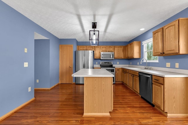 kitchen featuring dark wood-type flooring, a kitchen island, a sink, baseboards, and appliances with stainless steel finishes