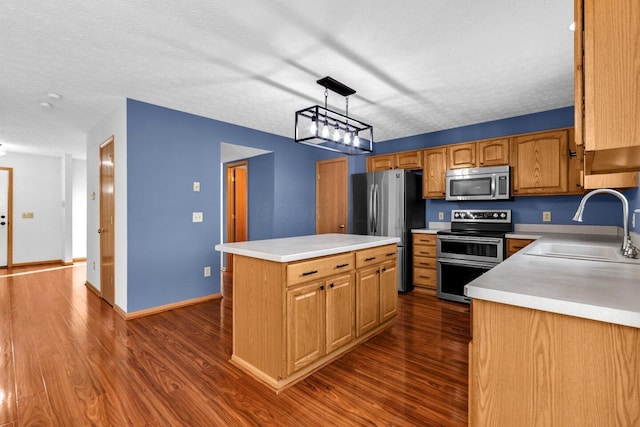 kitchen with light countertops, appliances with stainless steel finishes, dark wood-type flooring, a sink, and a kitchen island