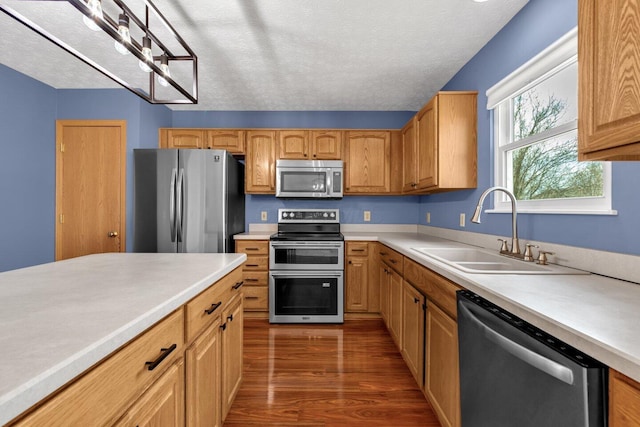 kitchen with dark wood finished floors, stainless steel appliances, light countertops, a sink, and a textured ceiling