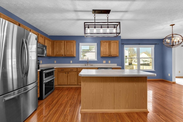 kitchen featuring wood finished floors, a kitchen island, a sink, light countertops, and appliances with stainless steel finishes