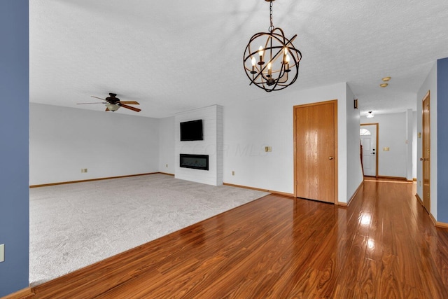 unfurnished living room featuring a large fireplace, a textured ceiling, baseboards, and wood finished floors